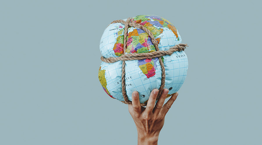 a young man holds an earth globe tied with rope, on a pale blue background, in a panoramic format to use as web banner or header