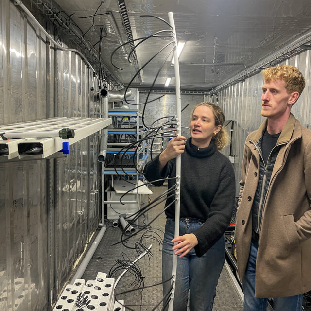 Iris Madsen og Jacob Copeland fra Hydrovertic viser deres vækstcontainer frem. Den er i gang med at blive gjort klar. Iris viser her et vandingssystem til planterne. 